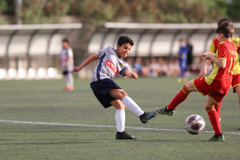 تصویر هیجان انگیز از بازی دو فوتبالیست نوجوان در زمین چمن یکی با لباس قرمز و دیگری با لباس طوسی و آرم روستوف ایران